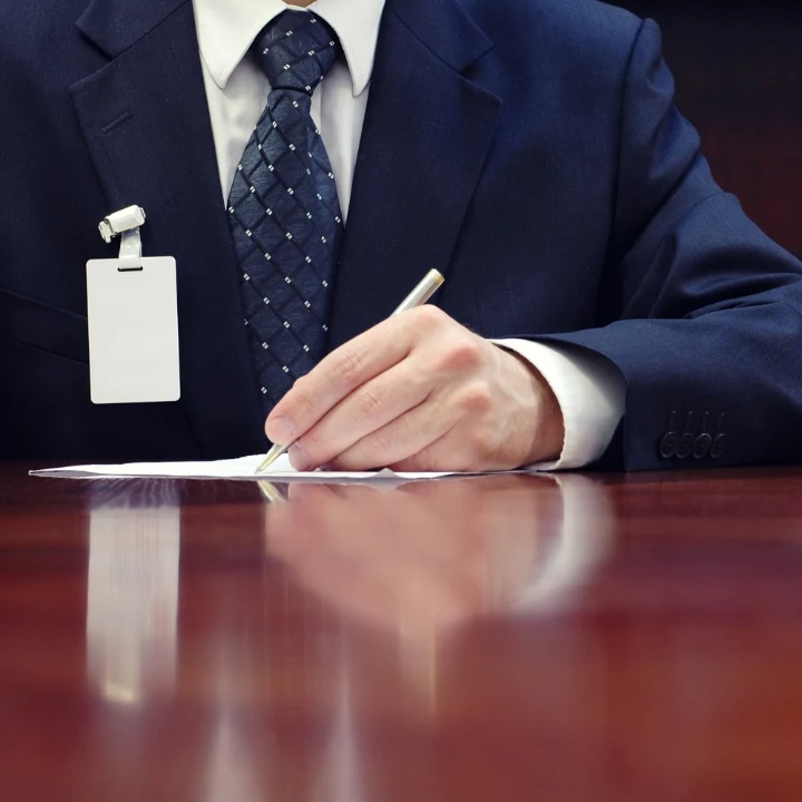 Mężczyzna podpisujący wniosek o założenie firmy. Na zdjęciu widoczny meżczyzna ubrany w ciemno granatowy garnitur podpisujący dokuementy.